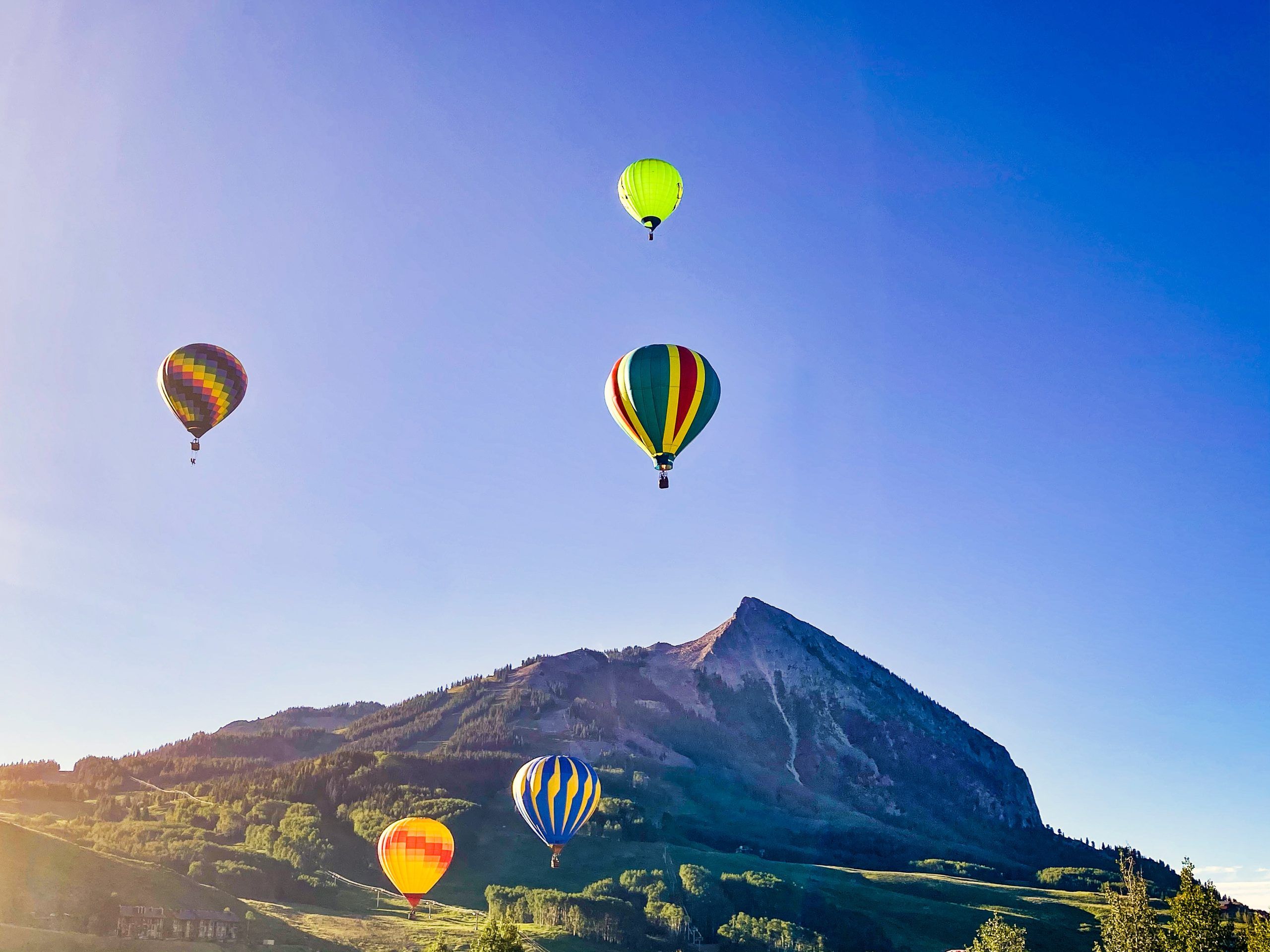 Hot air balloons float in a blue sky above Crested Butte on a summer morning.