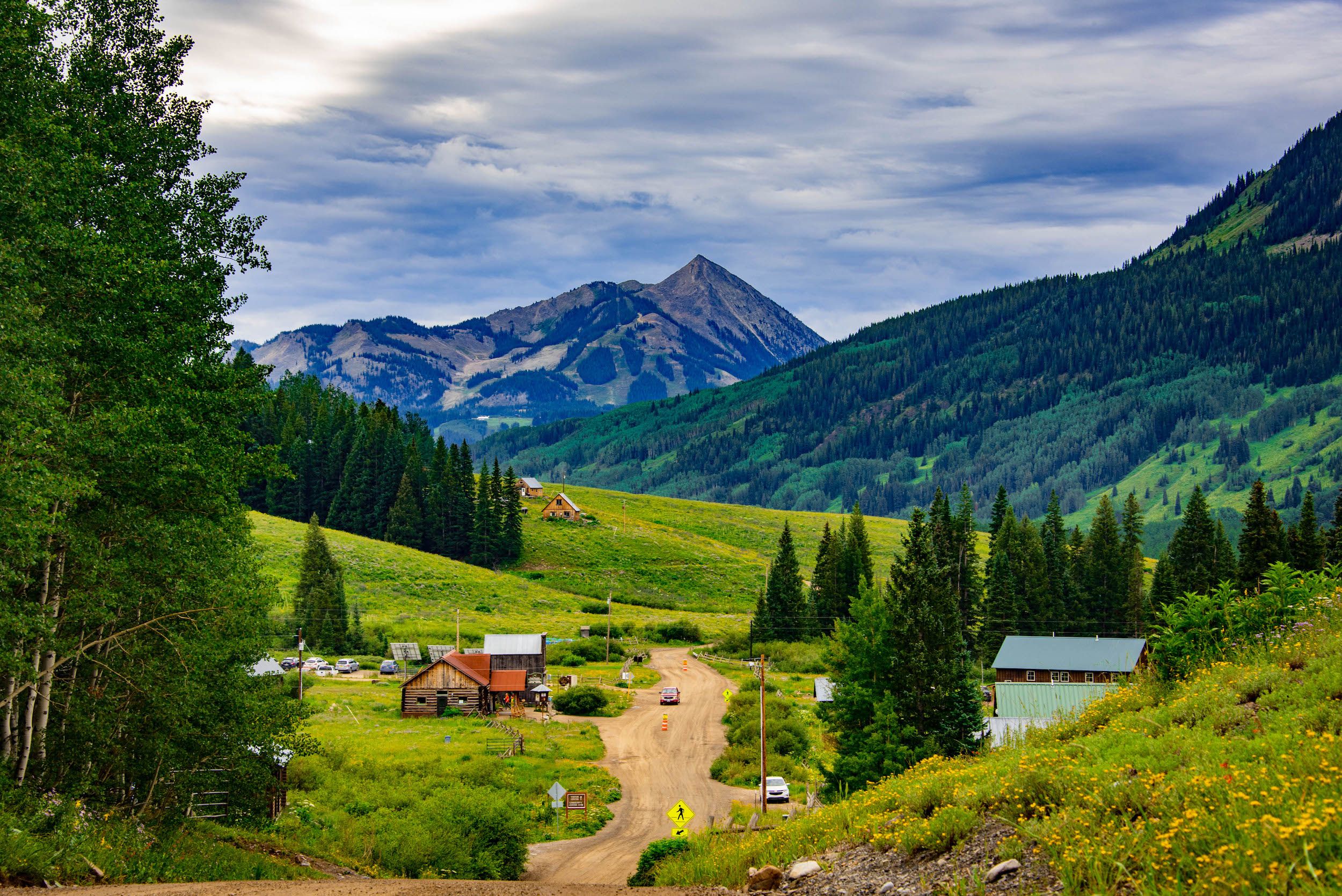 a small collection of buildings along a dirt road with a pointy mountain peak in the background. It is the rocky mountain biological laboratory. 
