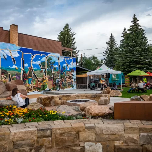 A downtown park with a mural on the wall, tents set up and someone playing music on a stage