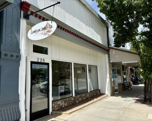 The exterior of Gunnison Jerky Co and Colorado Mercantile. The building has four windows and a sign hanging above the door.