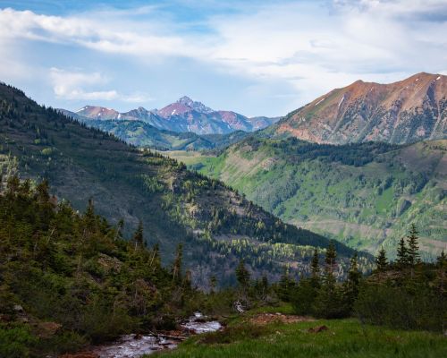 a mountain view of the maroon-bells crested butte to aspen hike. There are a few pointy mountain peaks in the background of a stream