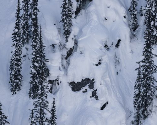 A stock photo from a previous Natural Selection tour competition. A snowboarder rides over a cliff through technical terrain.