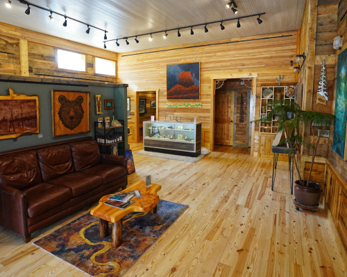 The interior of terrible mountain gallery in pitkin. the gallery is warm wood with a leather couch, colorful rug and plants. Paintings of nature and landscapes line the walls.