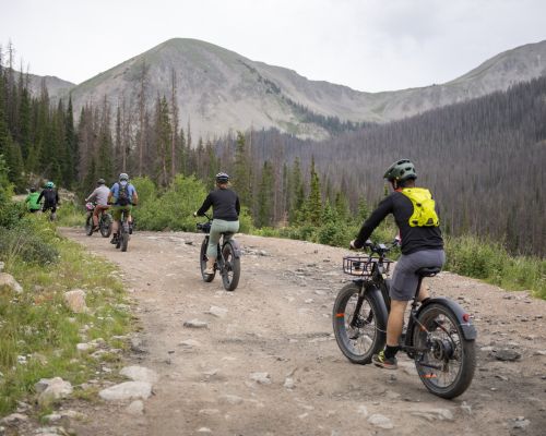 Six e-bike riders on a dirt road with mountain peaks in the background