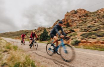 Three gravel bikers ride on a road next to orange rocks