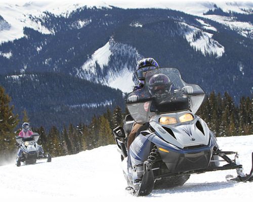 Two snowmobilers on a trail in Irwin, Colorado. This gentle climb is flanked by snowy hillsides and dense fir trees.