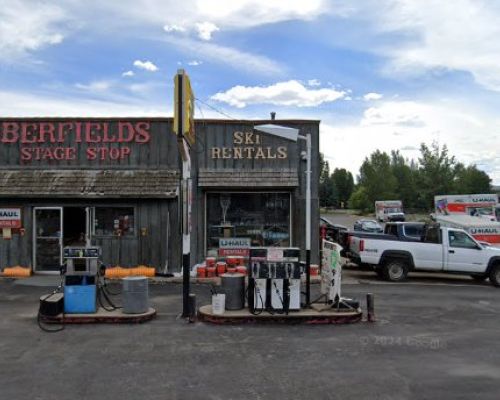 berfields stage shop gas station. A rustic building with the words "Berfields Stage Shop" across the top of the building exterior. An ice chest and gas jump sits in front of the building. Uhaul trucks are on the right side of the building.