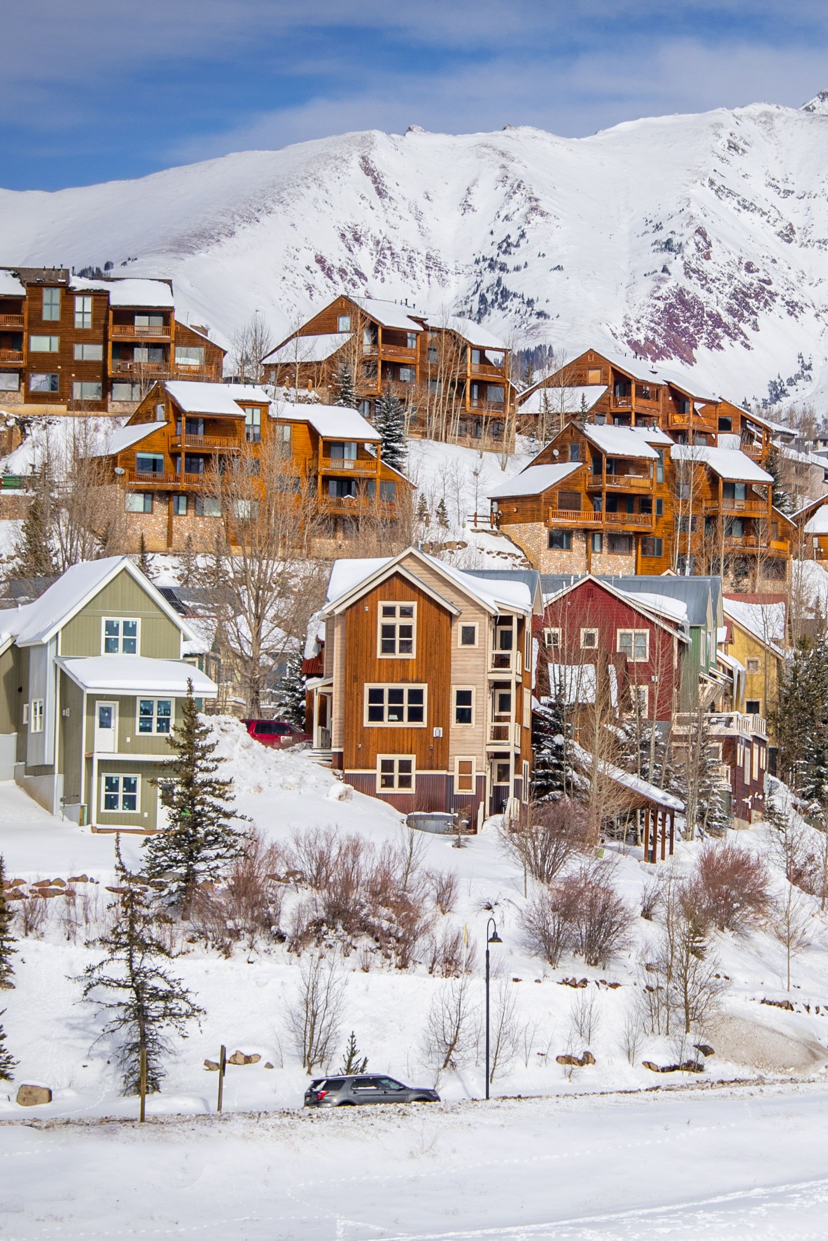 Snow-covered hotels sit upon a steep hill with large mountains in the background, in the town of Mt. Crested Butte, Colorado.