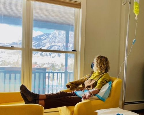 A woman relaxing in a plush chair by a window with a mountain view getting a treatment from Revive IV Spa in Crested Butte.