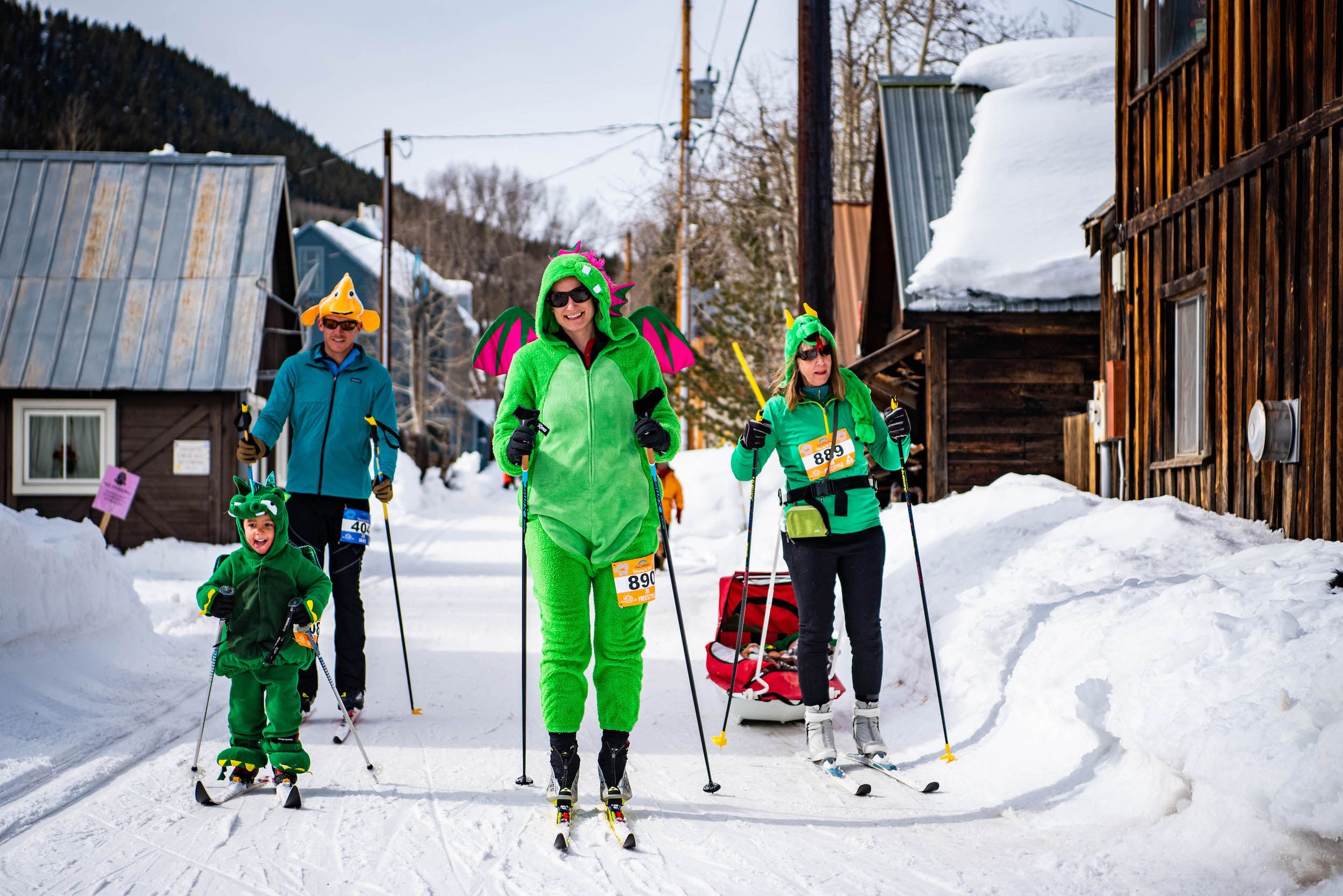 A group of people dressed like dinosaurs on skinny skis on a snowy road