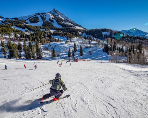 a skier heads down a slope with a pointy mountain peak in the background