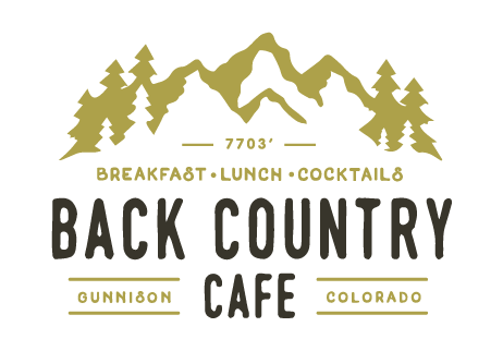 The outside of Back Country Cafe. A sign above the windows and doors reads "Back County Cafe Breakfast - Lunch - Cocktails." Two cafe tables sit under an umbrella where two men are sitting and talking.