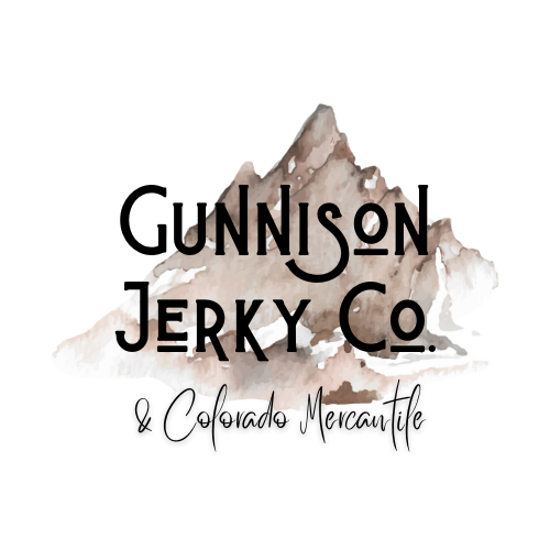The exterior of Gunnison Jerky Co and Colorado Mercantile. The building has four windows and a sign hanging above the door.