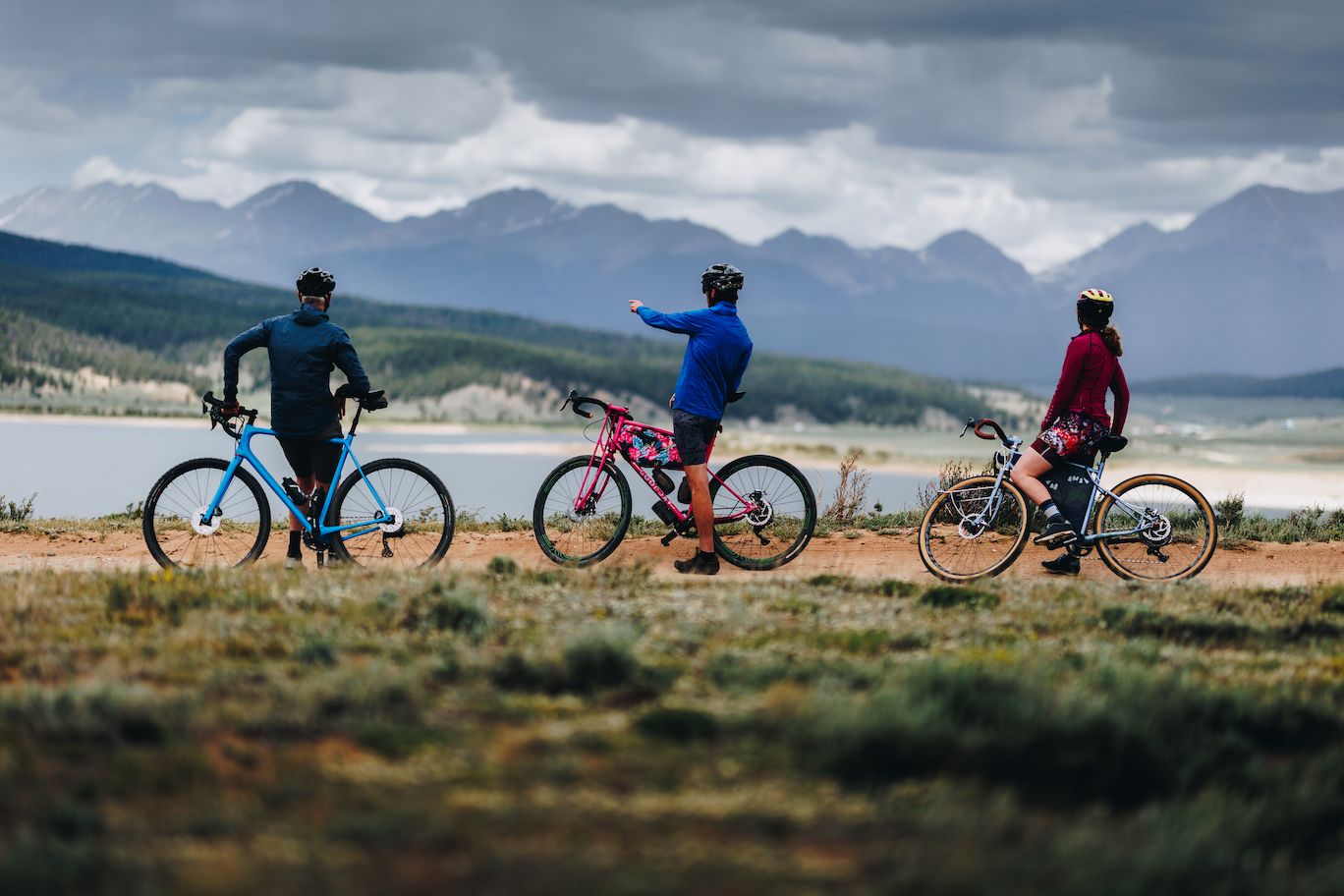 Three people stand with bikes and look at a view of mountains and a lake while graveling biking in Taylor Park