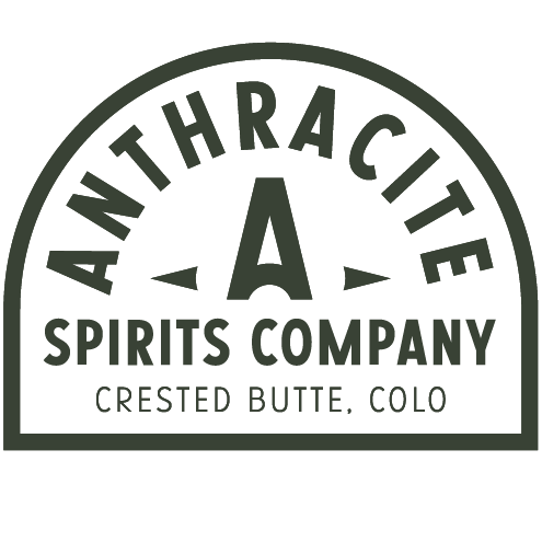 The bar at Anthracite Spirits. Four stools are sat in front of a bar top. Lights hang above the bar. Shelves with bottles of liquor are behind the bar.