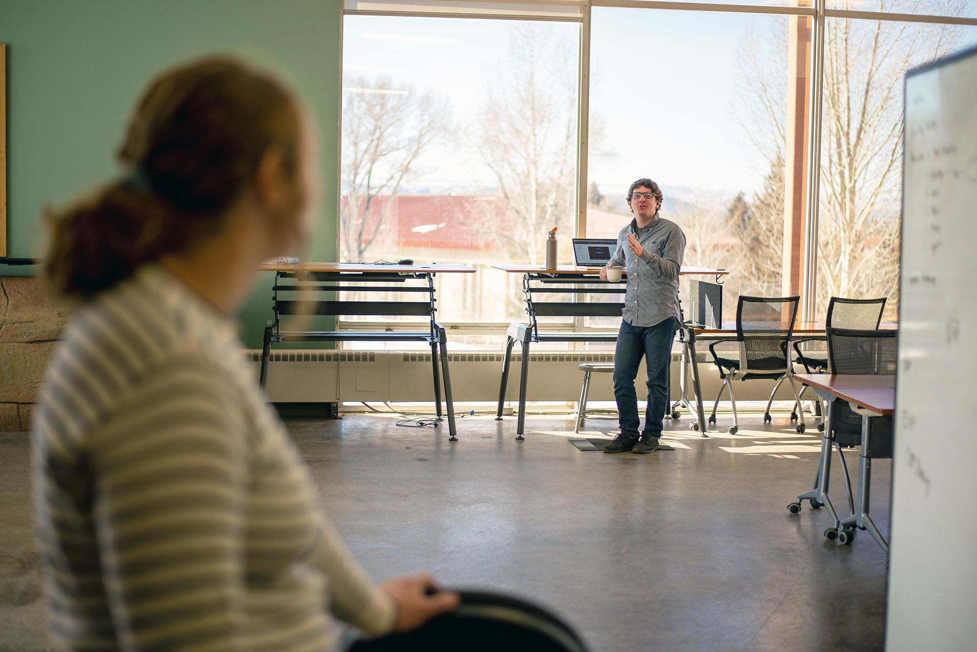 Two people talk across the ICELab @ Western, showing its amenities, including standing desks and whiteboards.