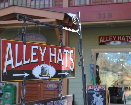 A sign that reads "Alley Hats" with two arrows and a line drawing of a top height. The sign is pointing towards the shop window and door.