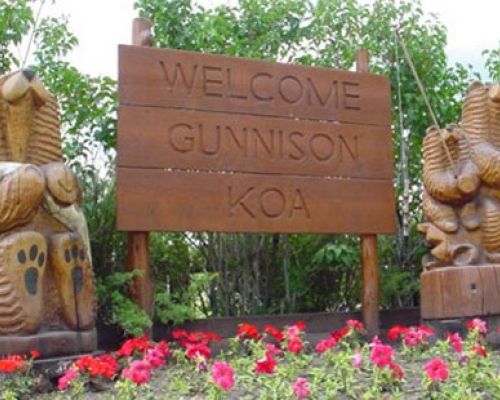 the sign for gunnison koa. Two large wooden bears stand on either side of a large wooden sign.