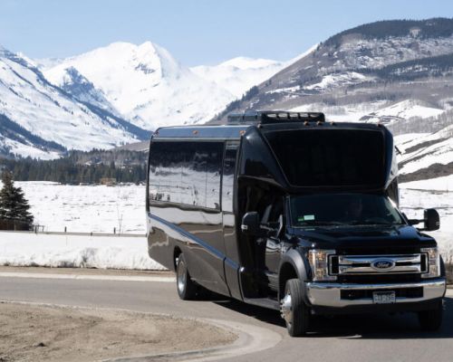 crested-butte-airport-transportation-alpine express. A large bus is parked on a road in front of snowcapped mountain peaks.