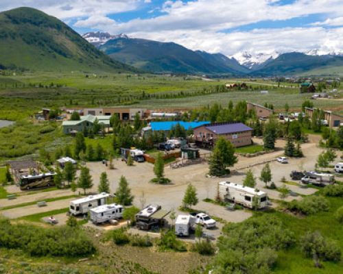 Crested Butte RV Resort in Crested Butte, CO. Mountain peaks loom in the background. RVs are parked at their designated campsites.