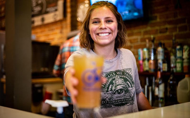 A woman hands a customer a beer over the bar at Doubleshot in Gunnison.