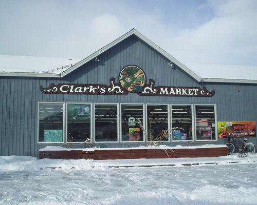 Clarks Market in Crested Butte, CO. The building has a peaked roof above a sign that says "Clark's Market." Seven large windows are under the sign.