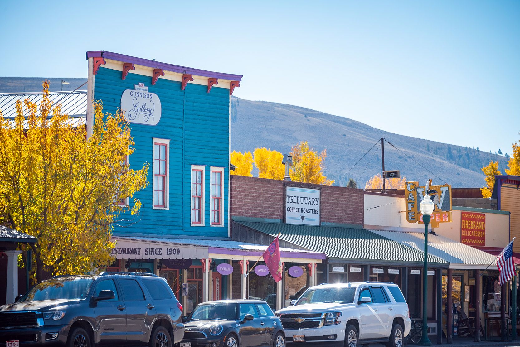 Trees with yellow leaves and bright storefronts line the street in downtown Gunnison, Colorado in fall.