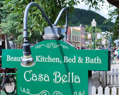 The sign for Casa Bella in Crested Butte, CO. The sign is rounded on the top and sticks out on the sides on top of a rectangular shape. The sign reads "Beauty in Kitchen, Bed & Bath Casa Bella"