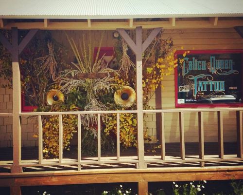 The store front of Calico Queen in Crested Butte. A simple wooden porch and porch rail is in front of a window that says "Calico Queen Tattoo."
