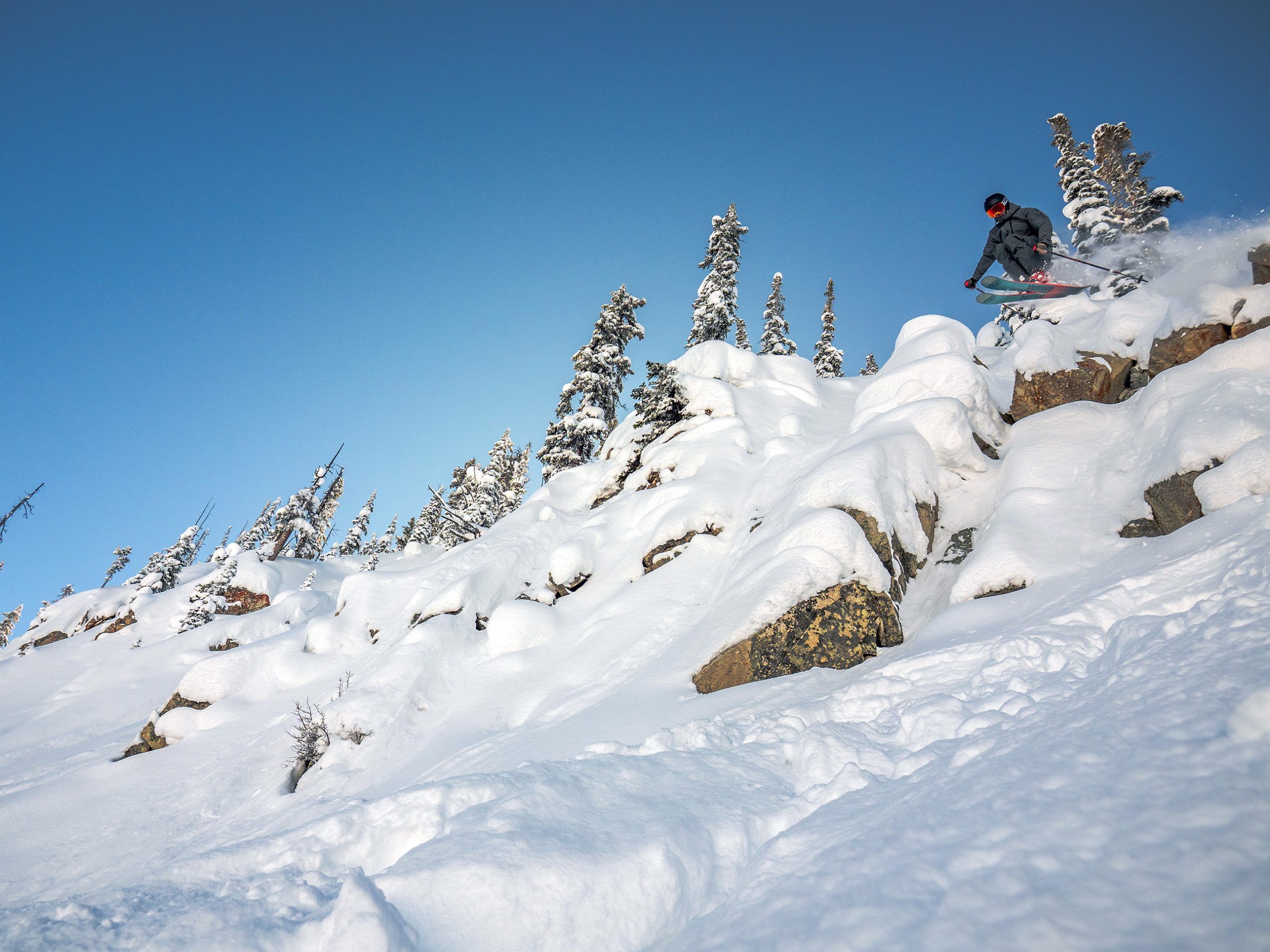 On a visit to Crested Butte, a skier jumps off a cliff band on a bluebird day.