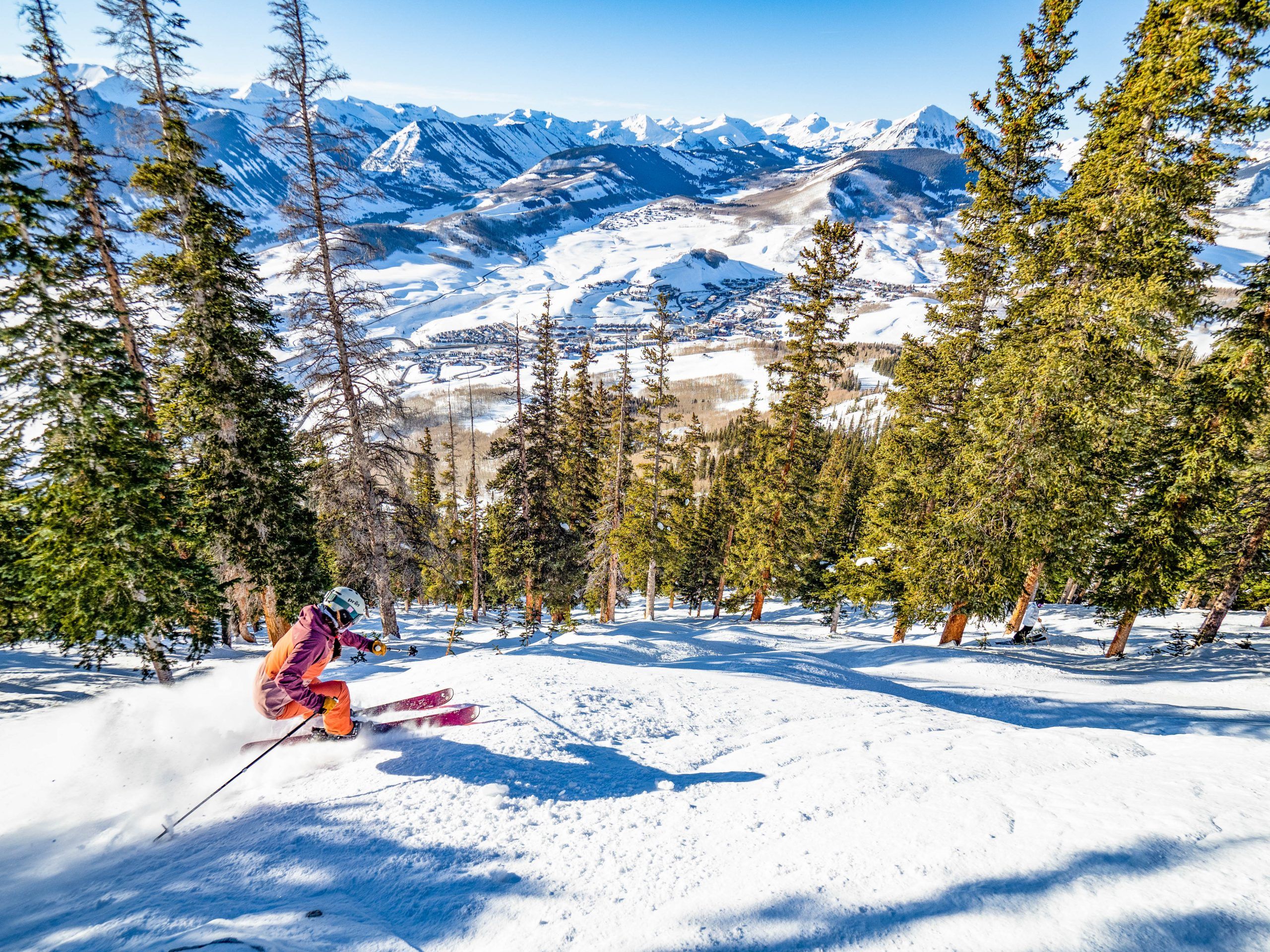 A woman skis on a steep off-piste run through conifer trees on a ski trip to Crested Butte.