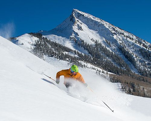 A skier on a steep slope with a pointy mountain peak in the background.