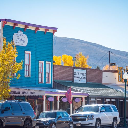 Trees with yellow leaves and bright storefronts line the street in downtown Gunnison, Colorado in fall.