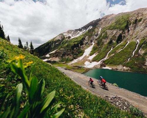 Three people ride bikes on a dirt road next to a lake