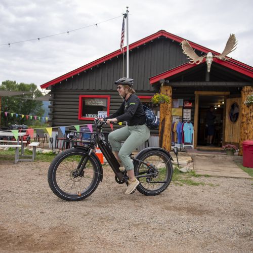 a woman riding a bike in front the stumbling moose lodge in pitkin co, a log cabin-style building with moose antlers mounted above the door