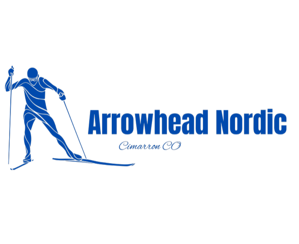A cross-country ski track at Arrowhead Nordic. Parallel dips in the snow are the classic ski track. Corduroy snow is for skate skiing. Mountains and pine trees are in the distance under a cloudy sky.
