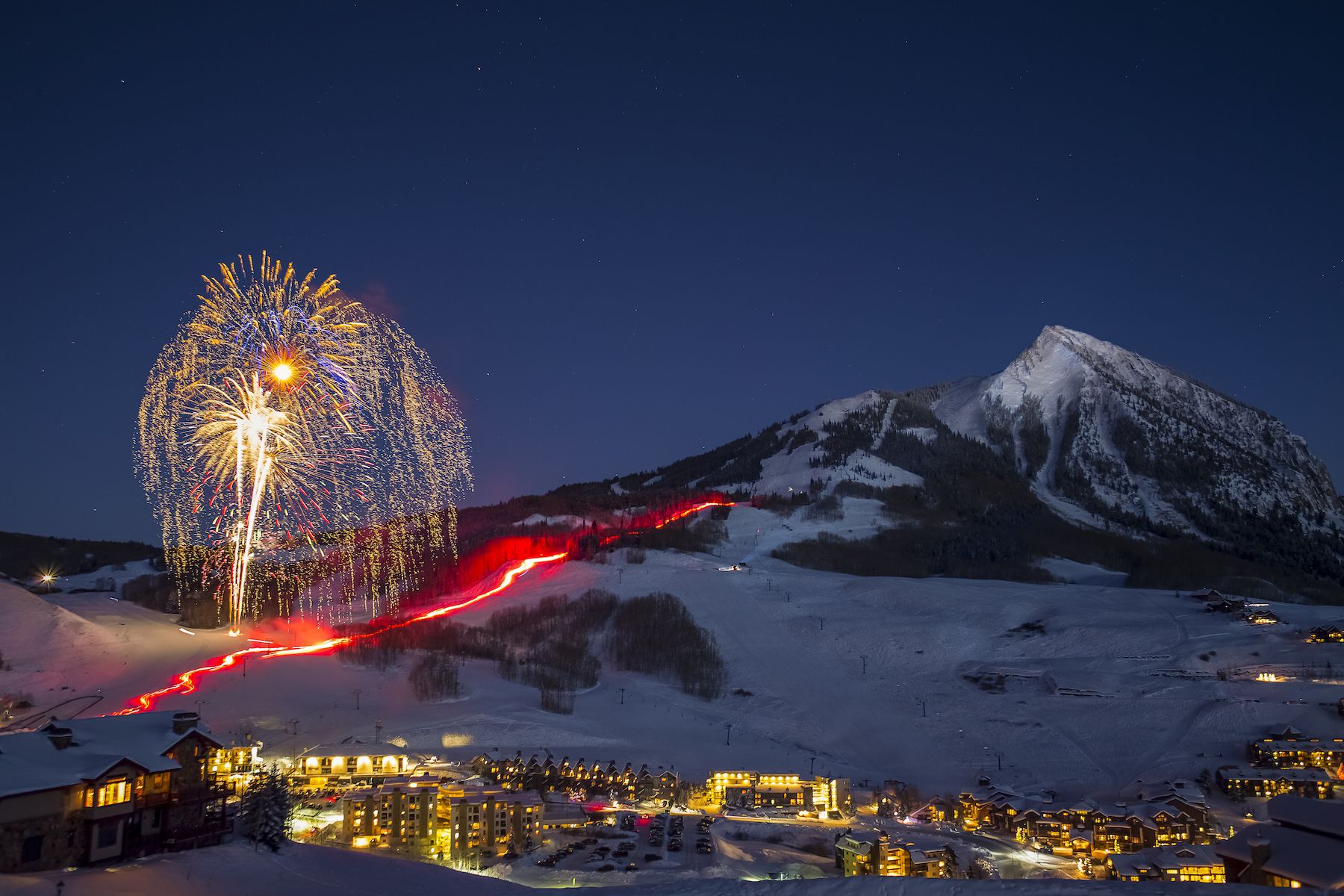 Skies skiing down a ski run while holding torches to create a line going down the mountain for the torchlight parade in Mt. Crested Butte