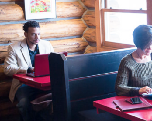 Two people sitting in separate booths on their laptops at Cement Creek Commons coworking space in CB South. A window is to the right.