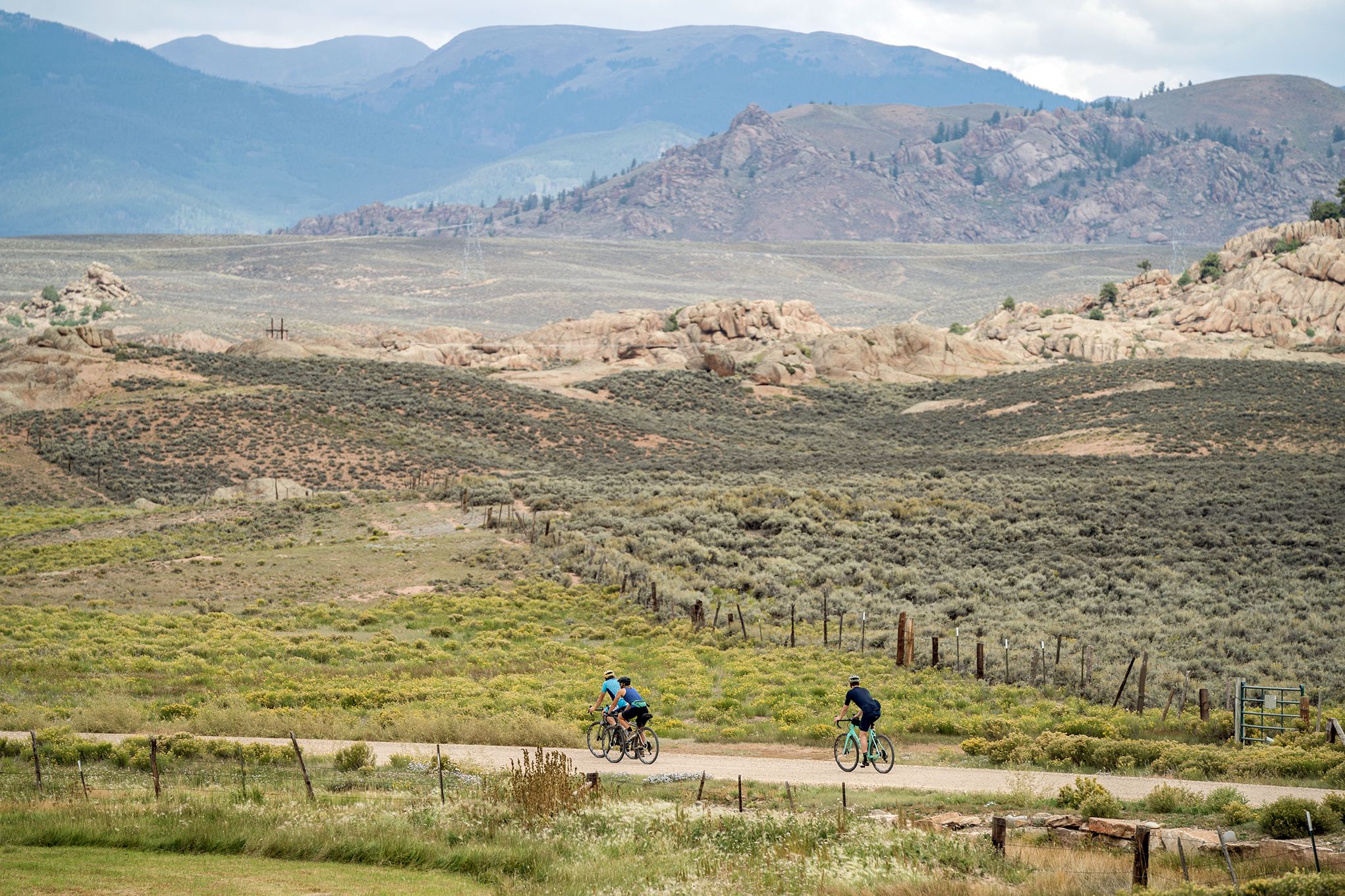 Three gravel bikers ride a gravel road in Gunnison with mountains in the background during Colorado vacation travel 