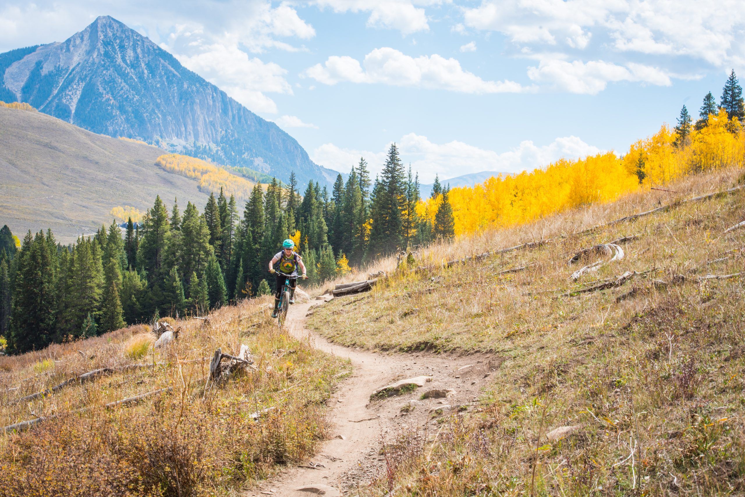 a mountain biker on a singletrack trail with a mountain peak in the background