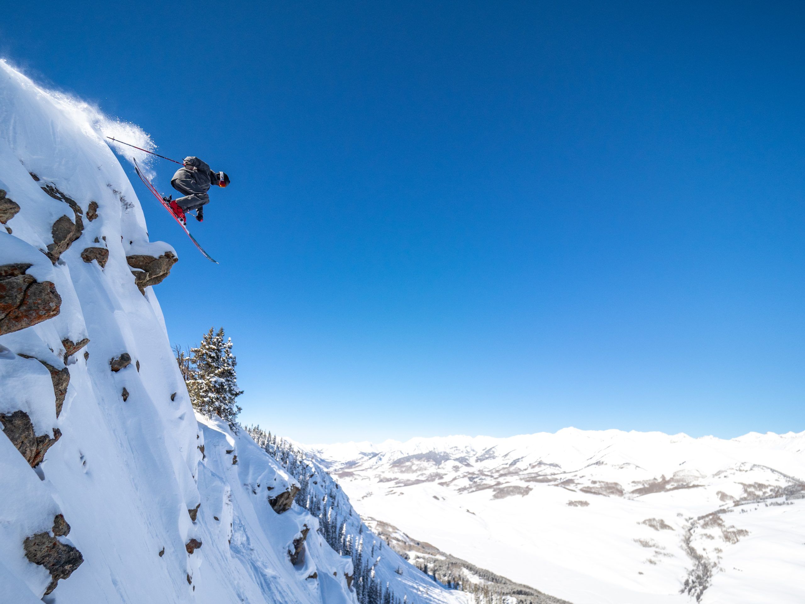 A skier blasts off a cliff in Highlife at Crested Butte on a bluebird day.