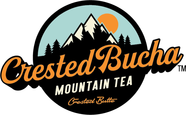 Bottles of Crested Bucha kombucha. Four bottles rest in a line. The bottles feature a circular logo with the words "Crested Bucha."