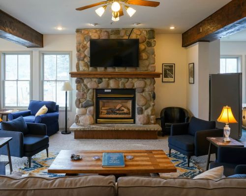 The interior of the Crested Butte Hostel. A cozy room features couches, chairs, end tables, lamps, bright windows and a fireplace.
