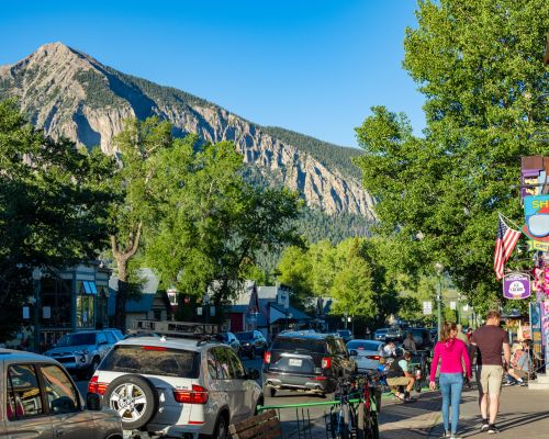 downtown crested butte. A high pointy mountain peak stands tall over a downtown area lined iwth trees, cars and storefronts.