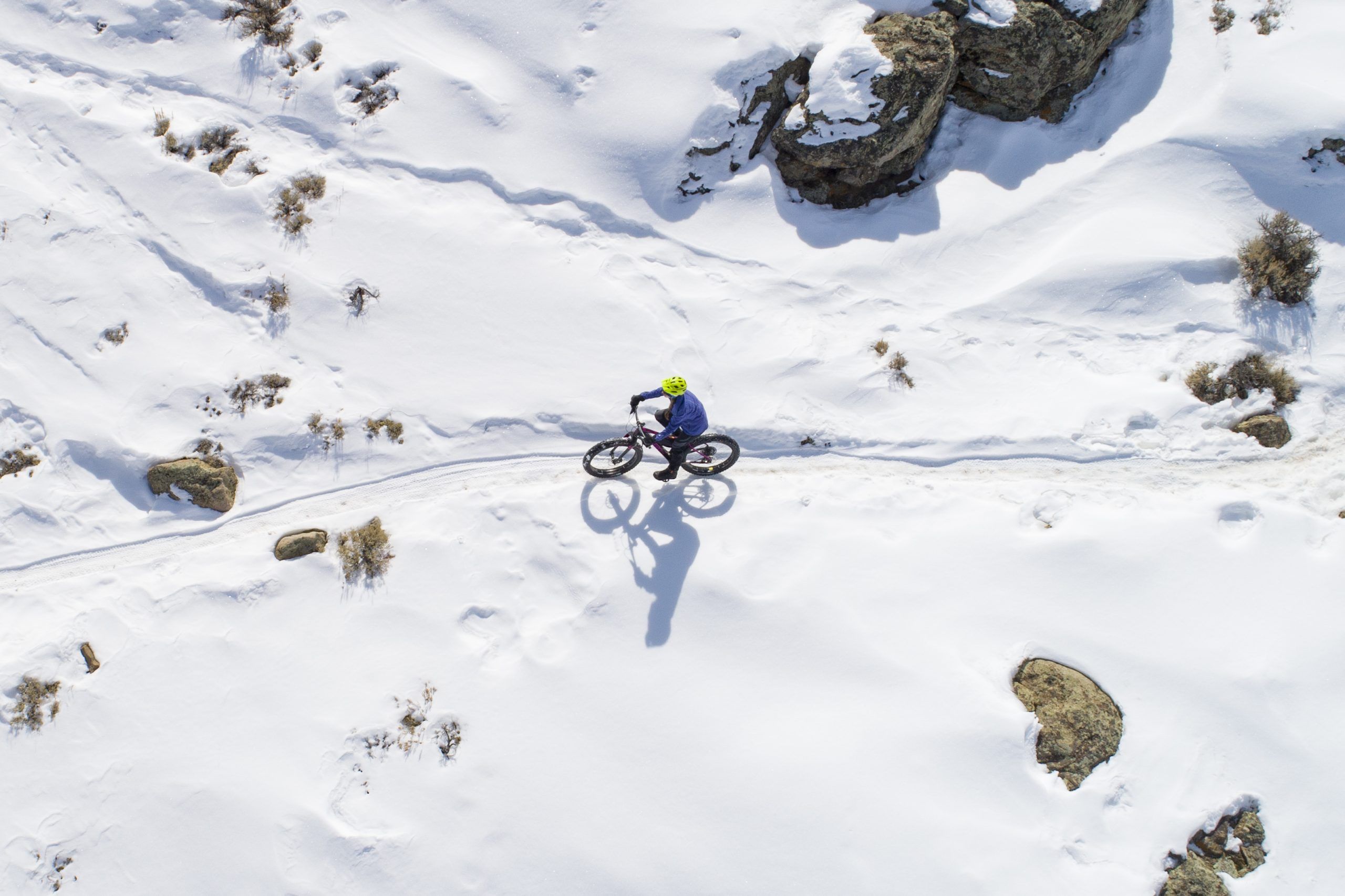 Someone rides a fat bike over a snowy, high desert landscape on a sunny day.