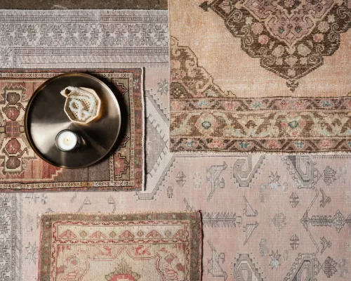 A gallery of artisan rugs from top down. The grouping of the rugs are overlaid with different patterns and colors. A brass tray with small items rests on the rugs