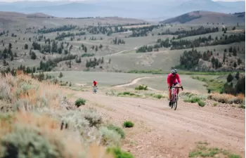 three gravel bikers ride on a gravel trail with rolling hills in the background