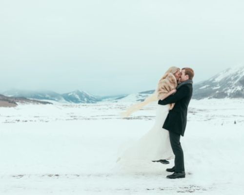 A picture from Cary Anne Photography in Crested Butte, part of Crested Butte Events. A groom is lifting his bride on a snowy landscape.