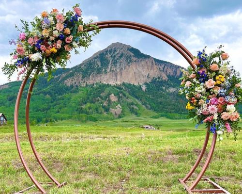 A round arbor with two bunches of flowers on it. The arch frames a view of a pointy mountain peak. crested+butte+wedding+and+event+florals+bramble+and+bloom