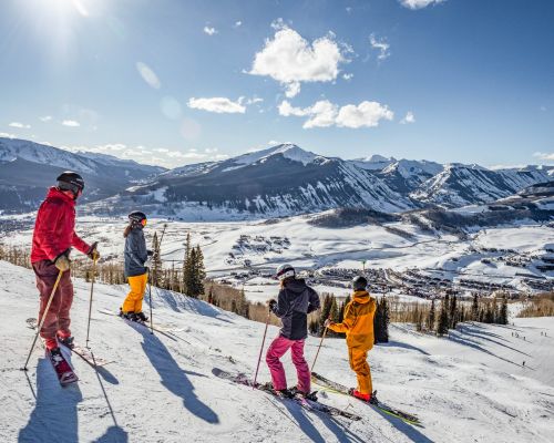 Four skiers at Crested Butte Mountain Resort take in the view of Crested Butte, Colorado from the top of a run